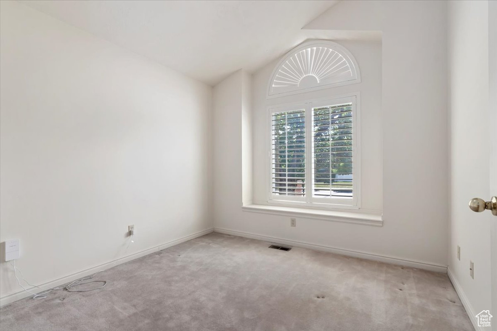 Carpeted empty room featuring baseboards and lofted ceiling