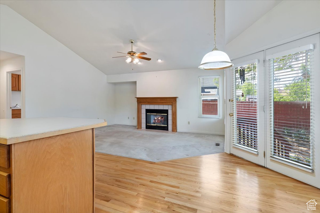 Unfurnished living room with vaulted ceiling, ceiling fan, light carpet, a tile fireplace, and light wood-style flooring