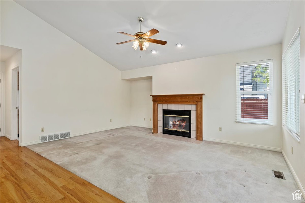 Unfurnished living room featuring a tile fireplace, lofted ceiling, ceiling fan, baseboards, and light carpet