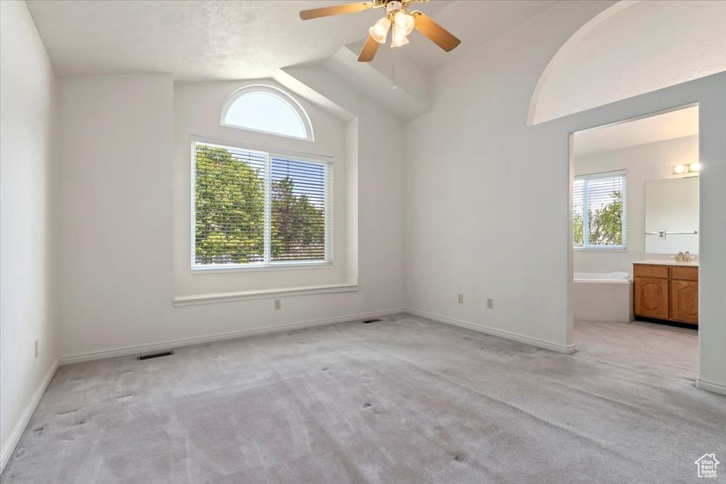 Unfurnished bedroom with vaulted ceiling, light colored carpet, baseboards, connected bathroom, and ceiling fan