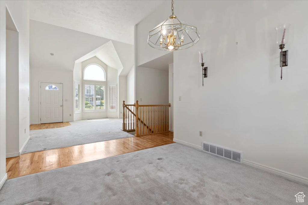 Carpeted entryway featuring a chandelier, baseboards, and high vaulted ceiling