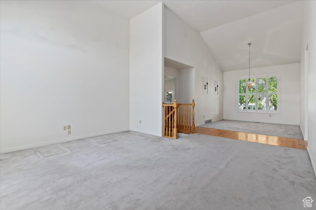 Carpeted empty room with high vaulted ceiling, baseboards, and a chandelier