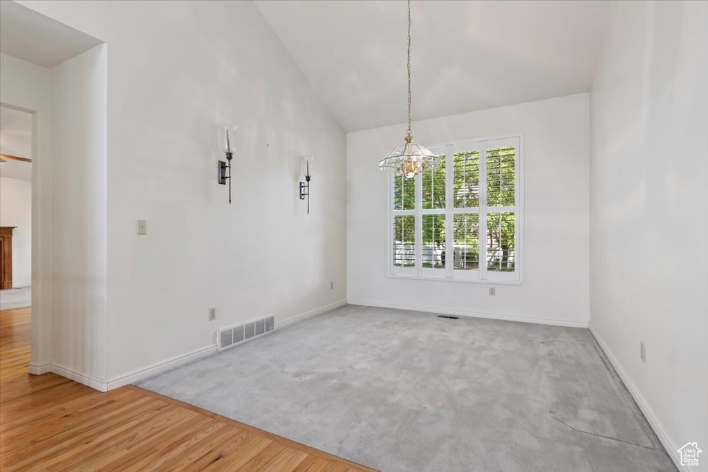 Unfurnished dining area featuring a chandelier, baseboards, carpet flooring, wood finished floors, and high vaulted ceiling