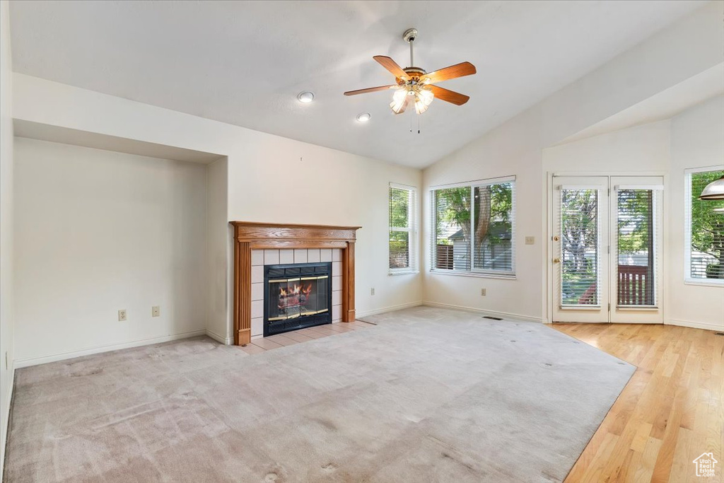 Unfurnished living room with healthy amount of natural light, a tile fireplace, lofted ceiling, a ceiling fan, and baseboards