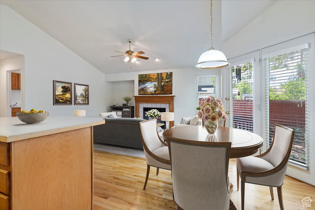 Dining room with vaulted ceiling, light wood-style flooring, a tiled fireplace, and ceiling fan