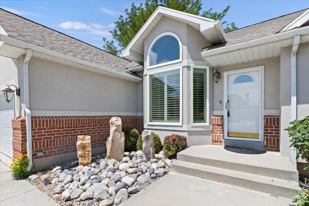 Property entrance featuring brick siding, a shingled roof, and stucco siding