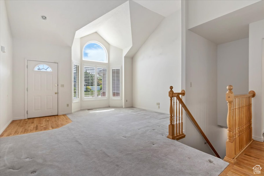 Carpeted foyer entrance with high vaulted ceiling and baseboards