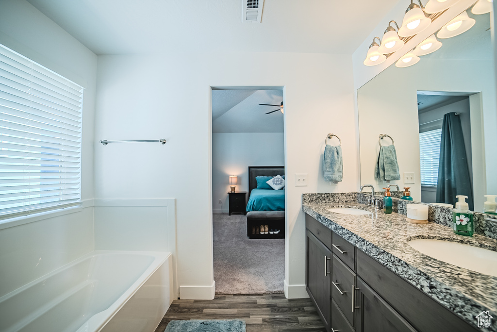Bathroom featuring ensuite bathroom, double vanity, a garden tub, wood finished floors, and a ceiling fan