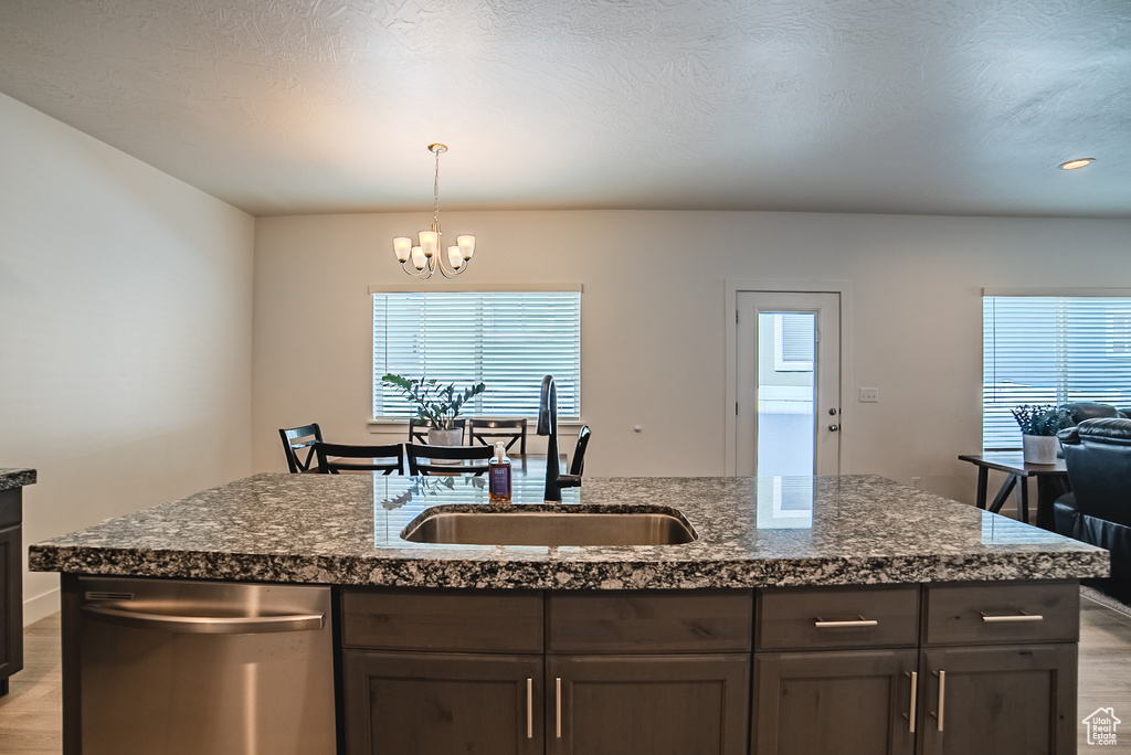 Kitchen featuring stainless steel dishwasher, a sink, light wood-type flooring, a chandelier, and dark brown cabinetry
