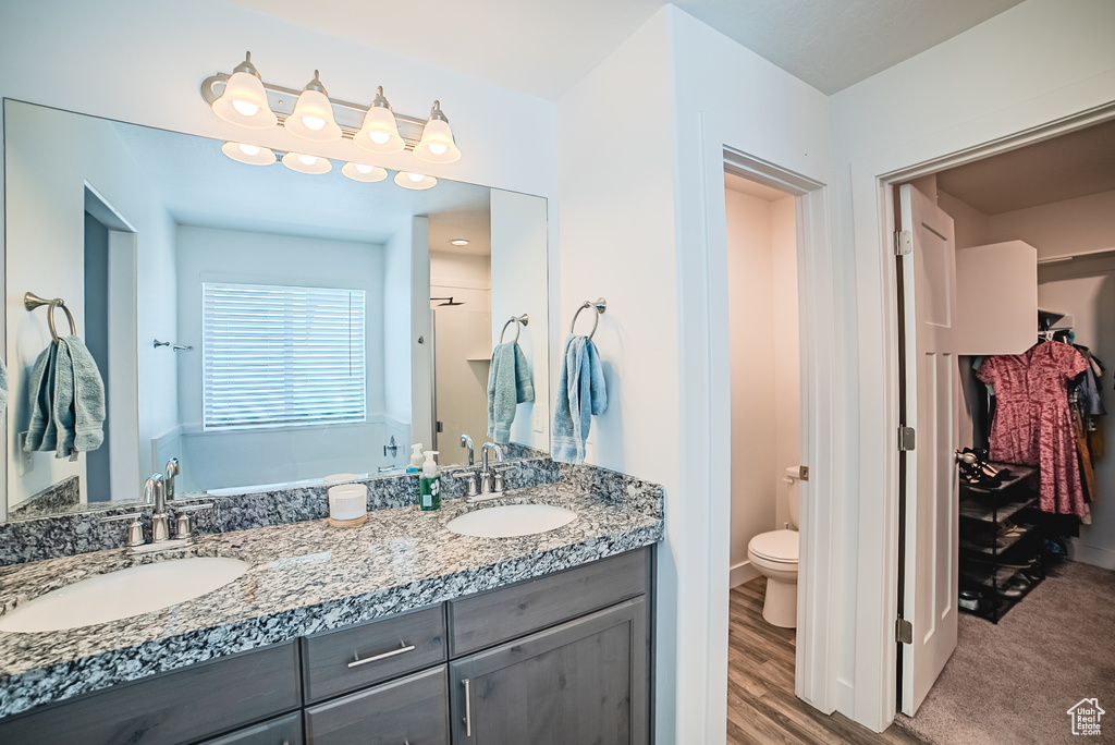 Bathroom with toilet, double vanity, a bath, a shower, and wood finished floors