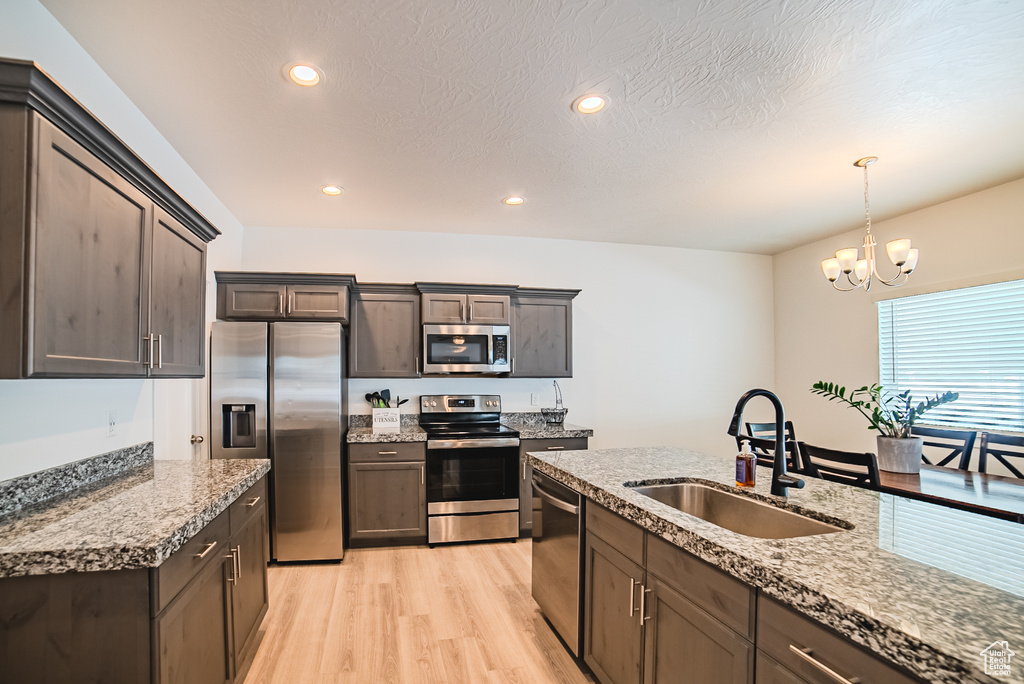 Kitchen with appliances with stainless steel finishes, a sink, light wood-style flooring, a chandelier, and pendant lighting