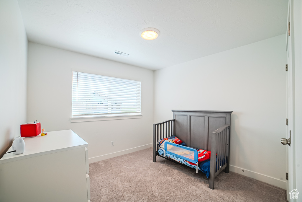 Bedroom featuring light carpet, baseboards, and a crib