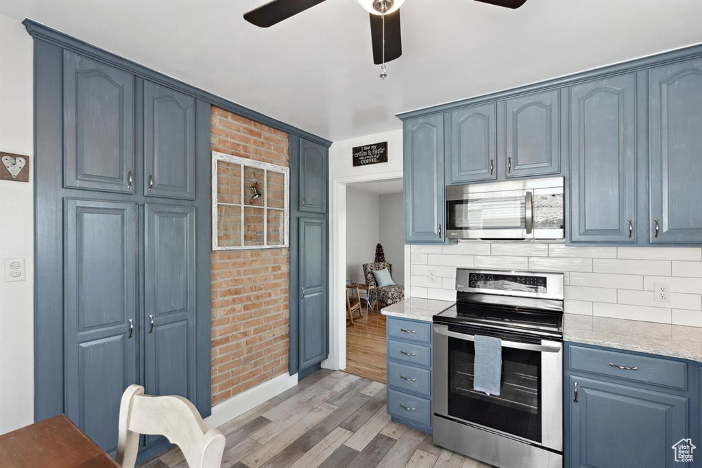 Kitchen featuring appliances with stainless steel finishes, light wood-style flooring, ceiling fan, blue cabinetry, and tasteful backsplash