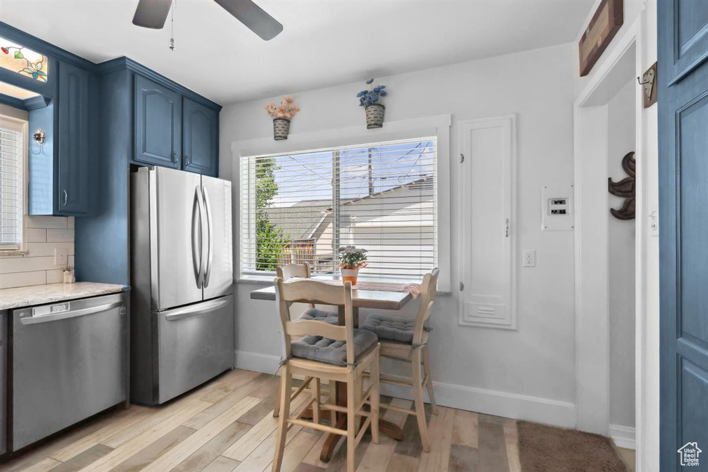 Kitchen with appliances with stainless steel finishes, blue cabinets, ceiling fan, light wood-style flooring, and baseboards