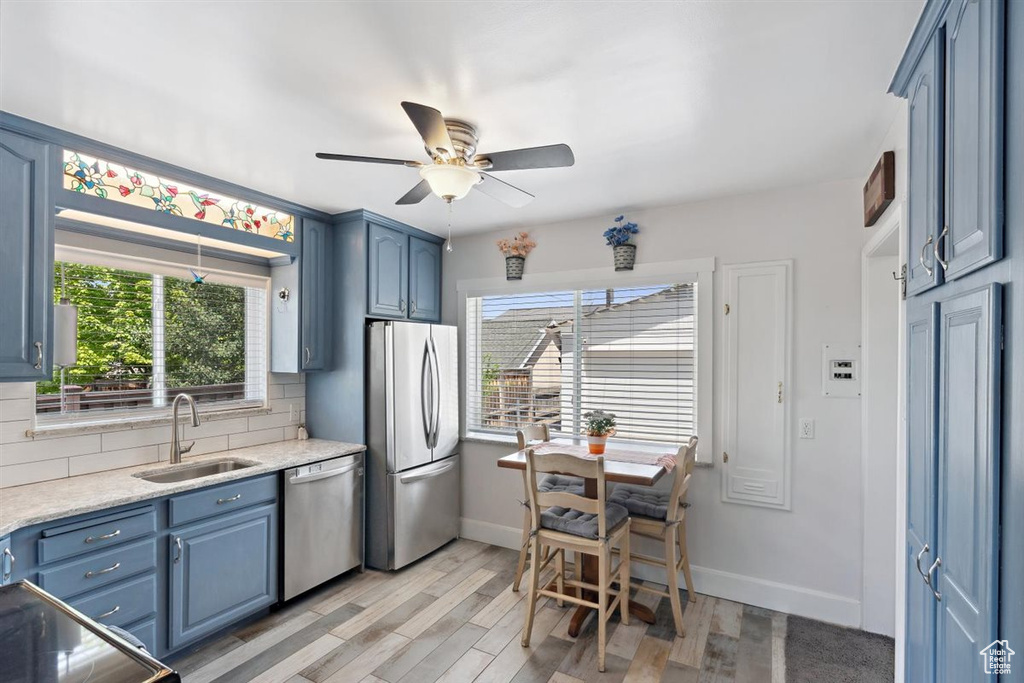 Kitchen with stainless steel appliances, a sink, blue cabinetry, light countertops, and tasteful backsplash