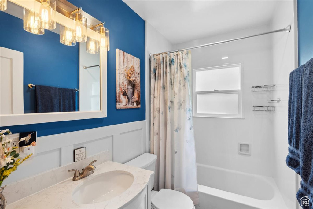 Full bathroom with toilet, vanity, shower / bath combo with shower curtain, wainscoting, and a chandelier