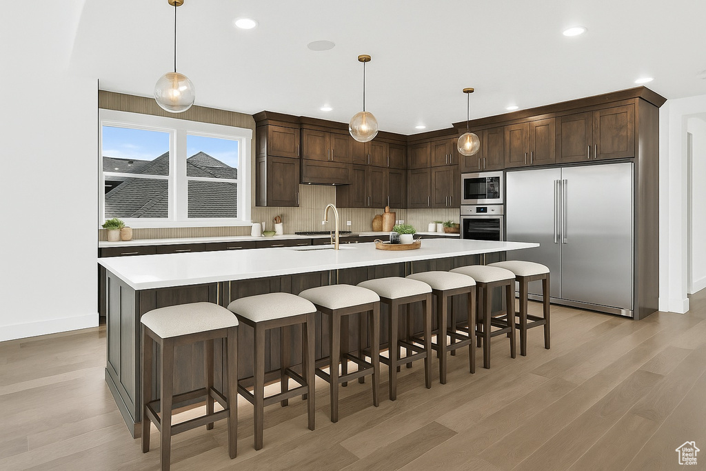 Kitchen featuring built in appliances, dark brown cabinetry, light wood-style flooring, light countertops, and recessed lighting