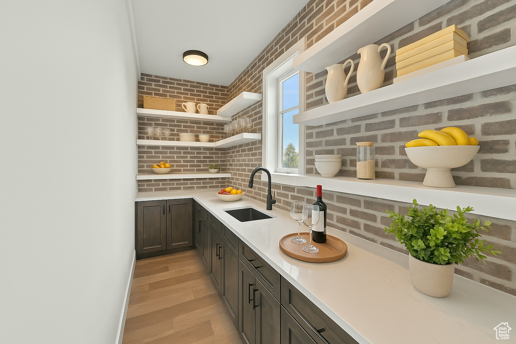 Kitchen with open shelves, a sink, light wood-style floors, light countertops, and brick wall