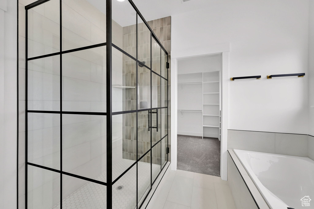 Bathroom featuring a garden tub, a tile shower, a walk in closet, and tile patterned flooring