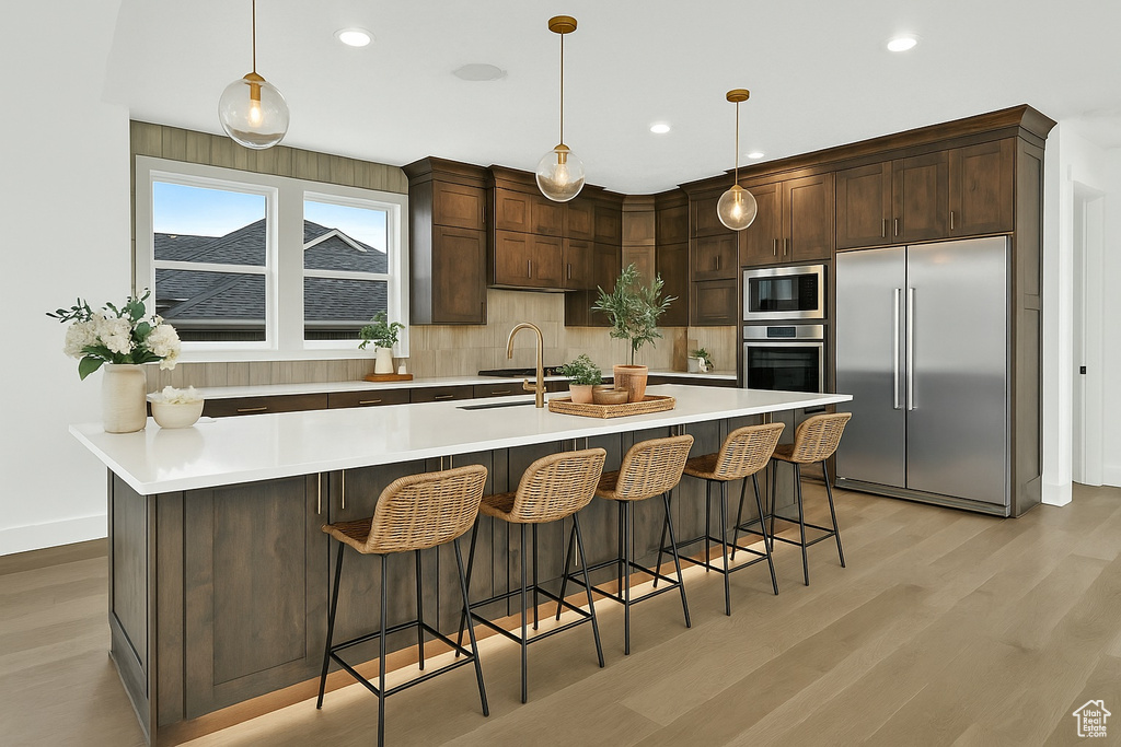 Kitchen featuring built in appliances, a sink, backsplash, light wood-style floors, and recessed lighting