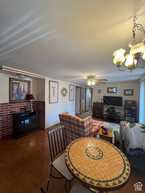 Dining space featuring ceiling fan, a chandelier, a textured ceiling, and a glass covered fireplace