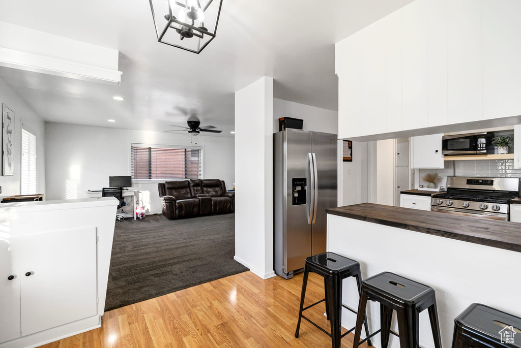 Kitchen with stainless steel appliances, butcher block countertops, a kitchen breakfast bar, white cabinets, and a ceiling fan