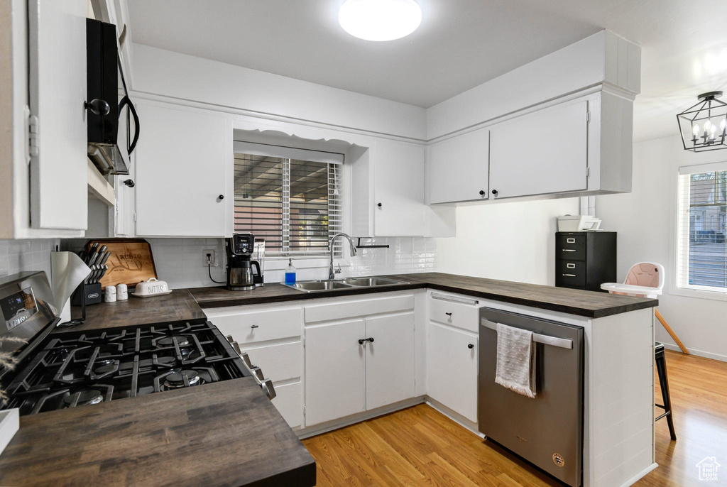 Kitchen featuring appliances with stainless steel finishes, a sink, decorative backsplash, and light wood finished floors