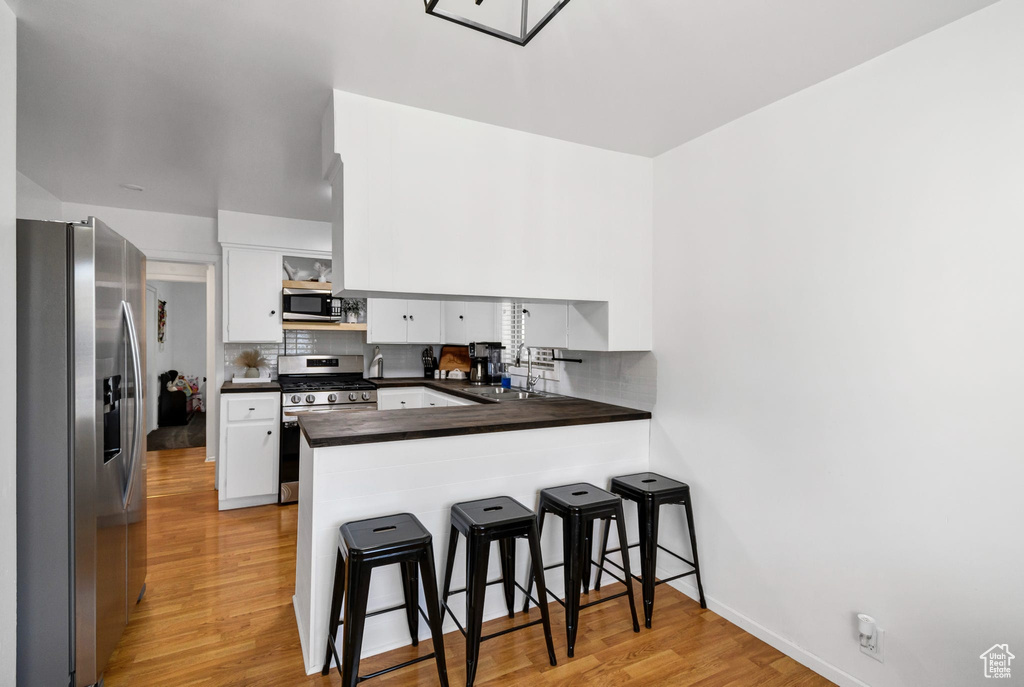 Kitchen featuring appliances with stainless steel finishes, dark countertops, a peninsula, light wood finished floors, and white cabinetry