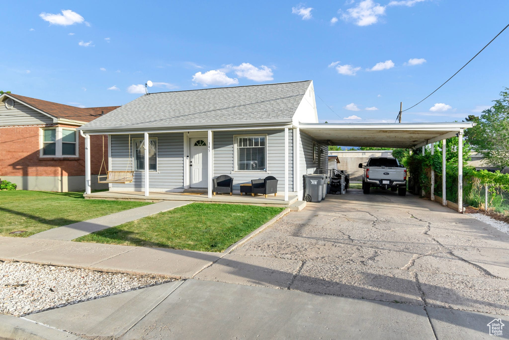 View of front of house featuring a front lawn, a carport, a porch, asphalt driveway, and a shingled roof
