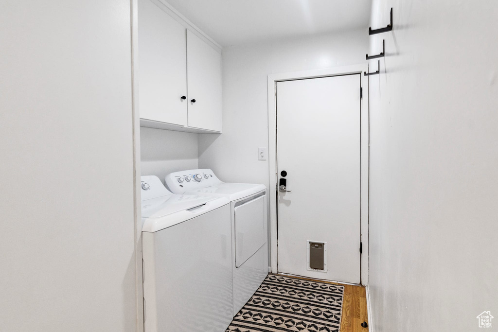 Washroom with washing machine and clothes dryer, cabinet space, and wood finished floors