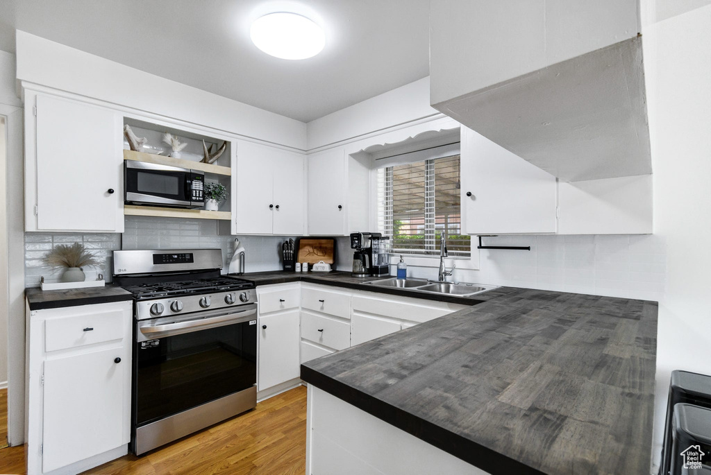 Kitchen featuring appliances with stainless steel finishes, a sink, dark countertops, white cabinets, and backsplash