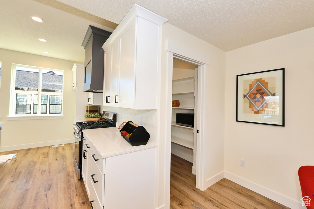 Kitchen with gas stove, light countertops, recessed lighting, white cabinets, and light wood-style flooring