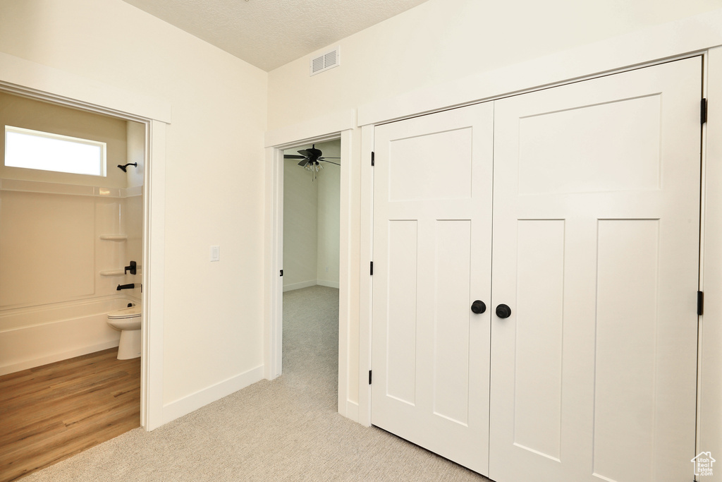 Unfurnished bedroom featuring light colored carpet, ensuite bath, baseboards, and a textured ceiling