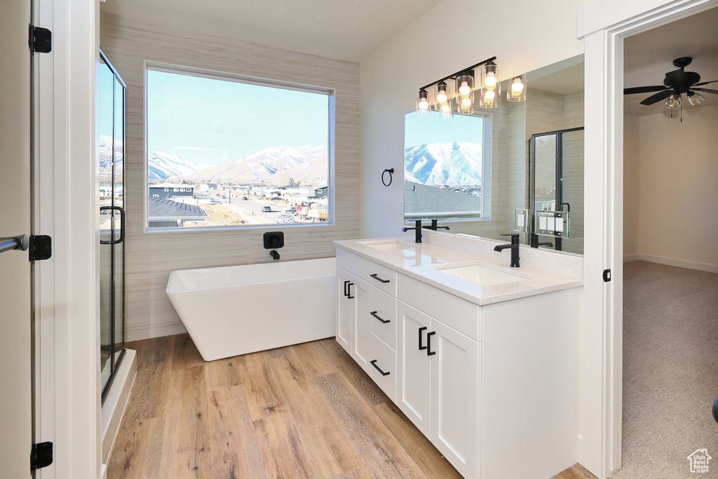 Full bathroom featuring a freestanding tub, double vanity, a stall shower, wood finished floors, and a ceiling fan