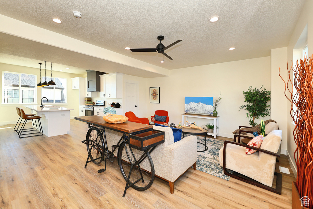 Living area featuring light wood-style flooring, recessed lighting, a textured ceiling, ceiling fan, and baseboards