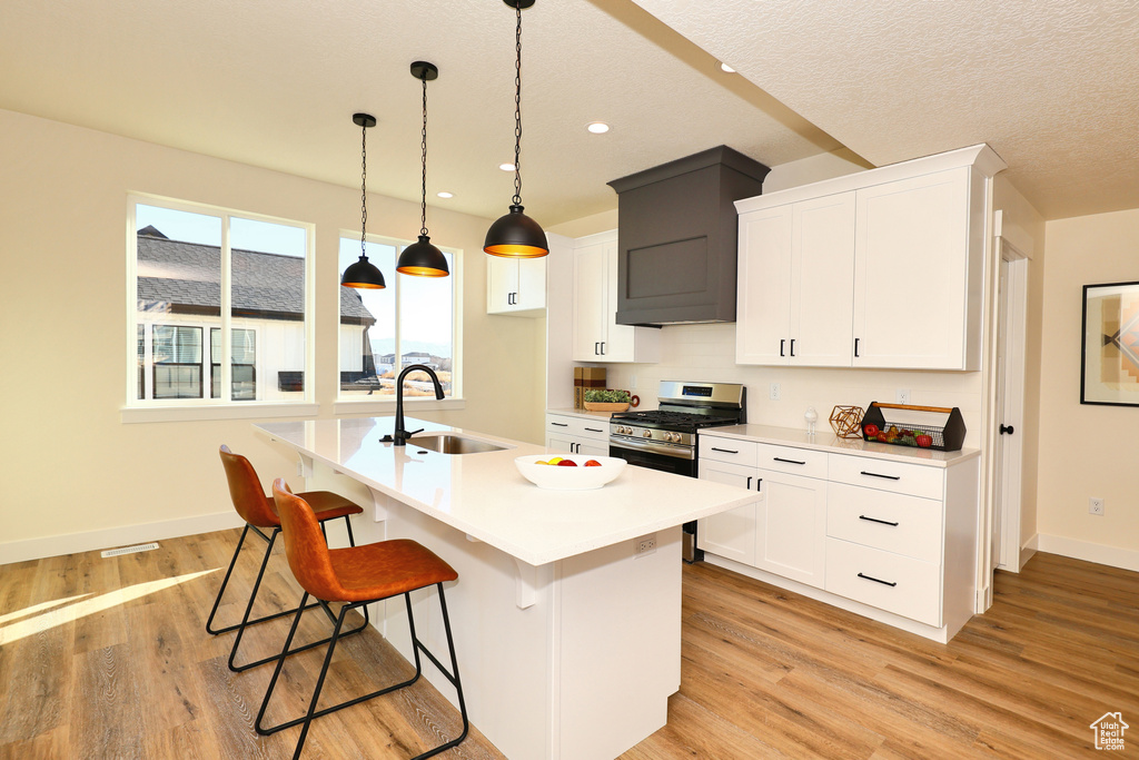 Kitchen featuring a sink, stainless steel gas range oven, baseboards, light countertops, and light wood-type flooring