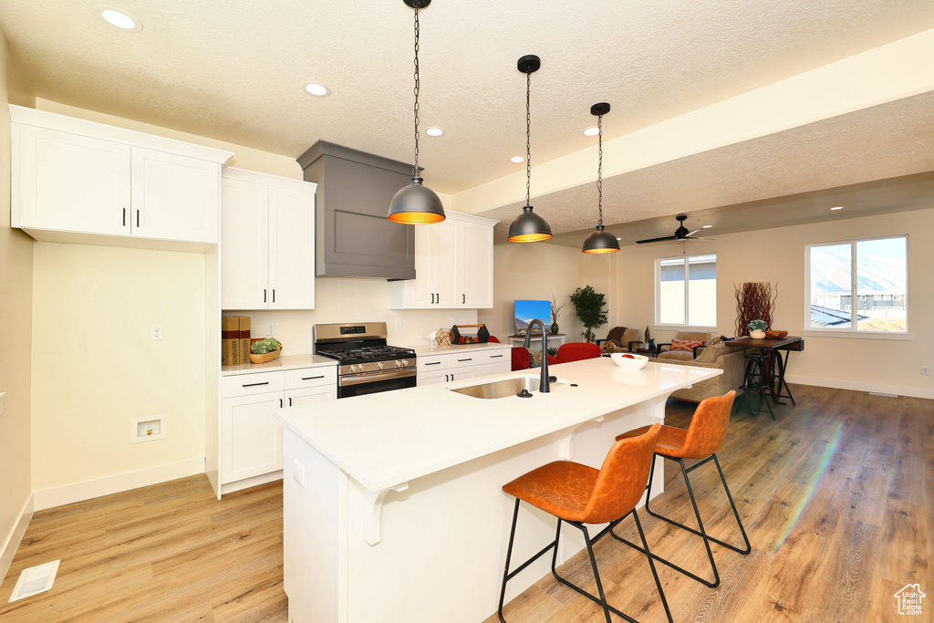 Kitchen with gas stove, a sink, a kitchen breakfast bar, light wood-style flooring, and a textured ceiling
