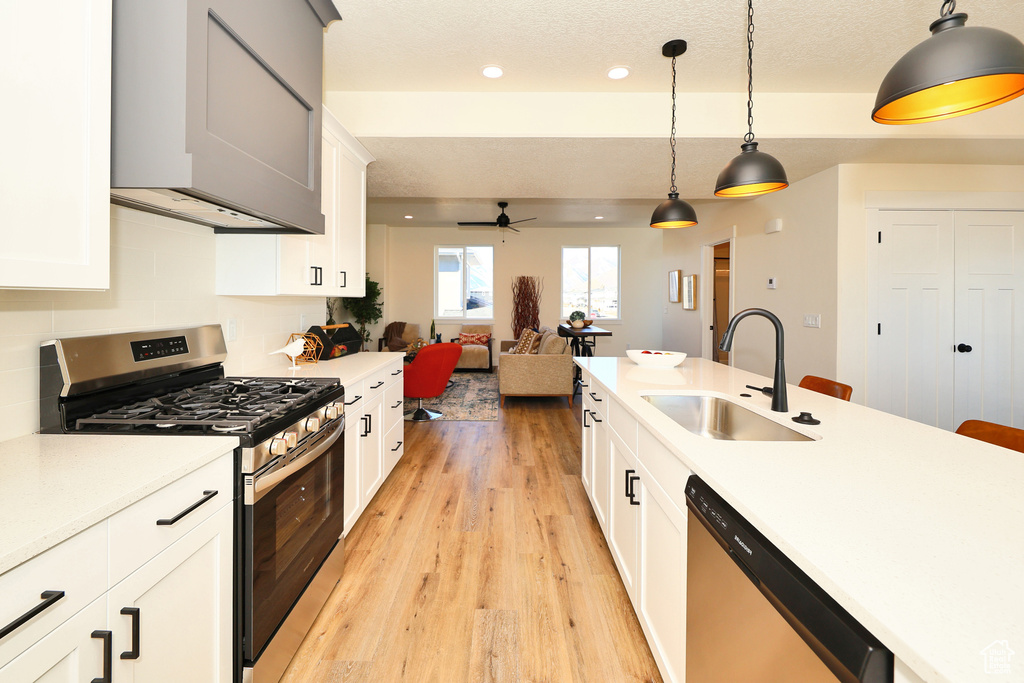 Kitchen with appliances with stainless steel finishes, a sink, light wood finished floors, ceiling fan, and hanging light fixtures