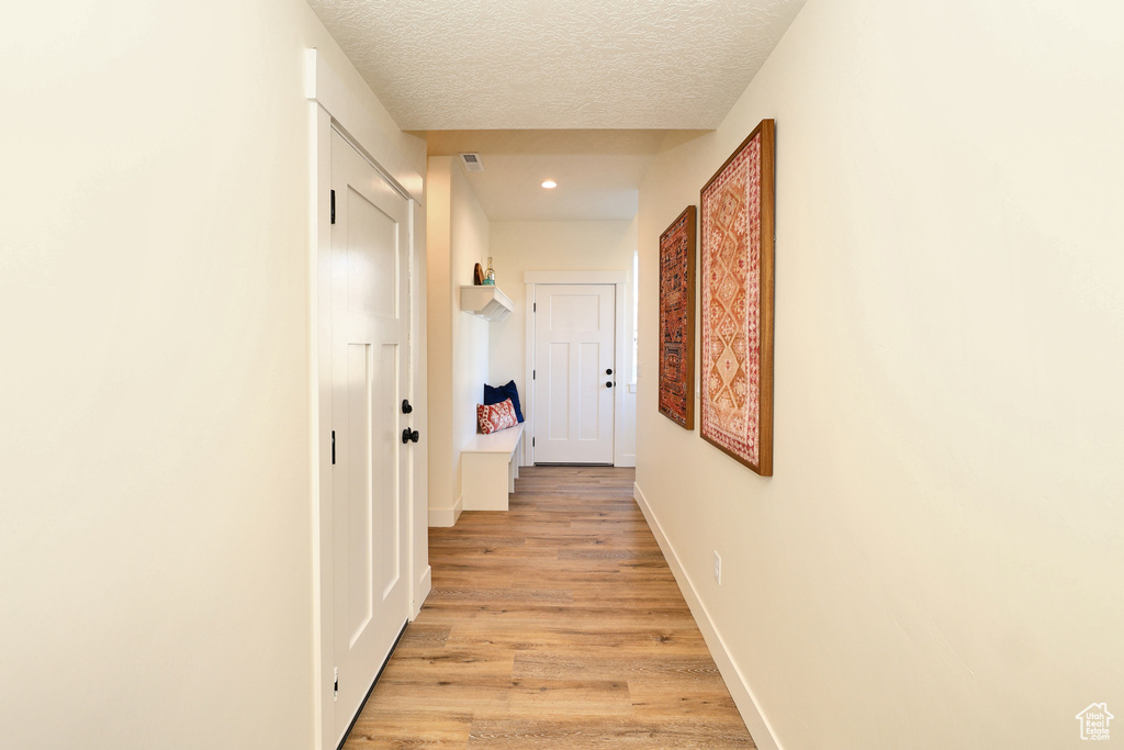 Corridor featuring light wood-type flooring, recessed lighting, a textured ceiling, and baseboards