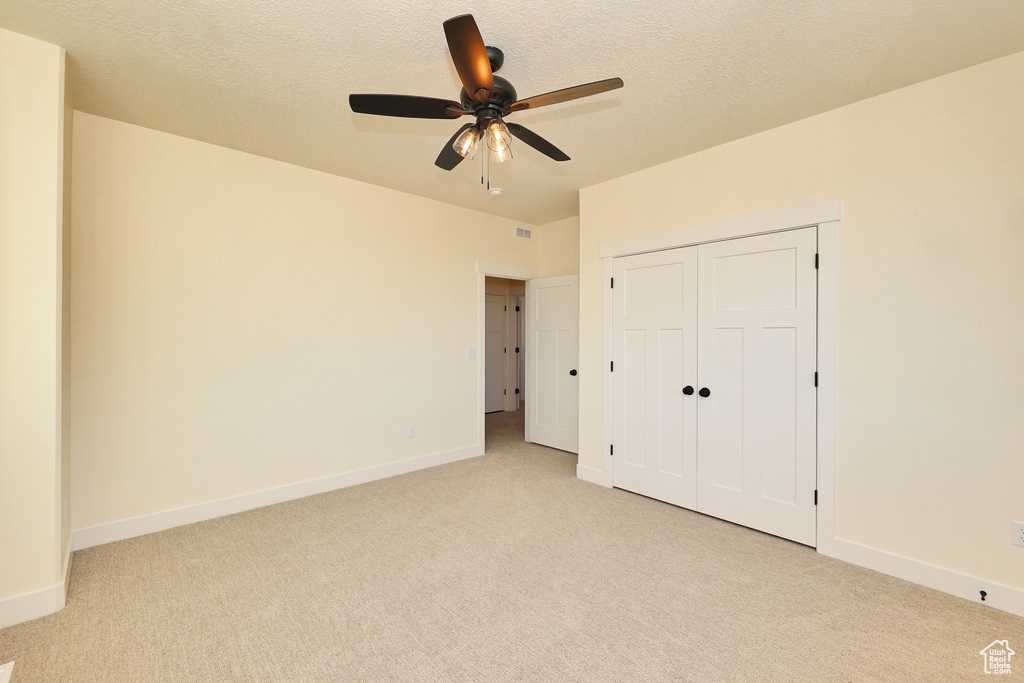 Unfurnished bedroom with light colored carpet, baseboards, a textured ceiling, and a closet
