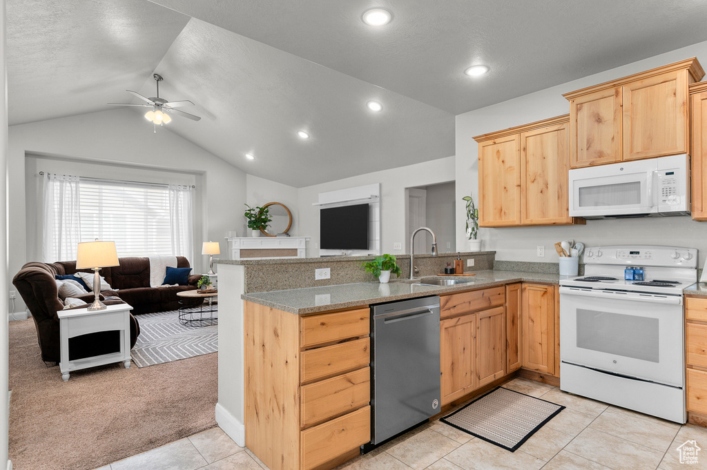 Kitchen featuring white appliances, a sink, open floor plan, light brown cabinets, and lofted ceiling