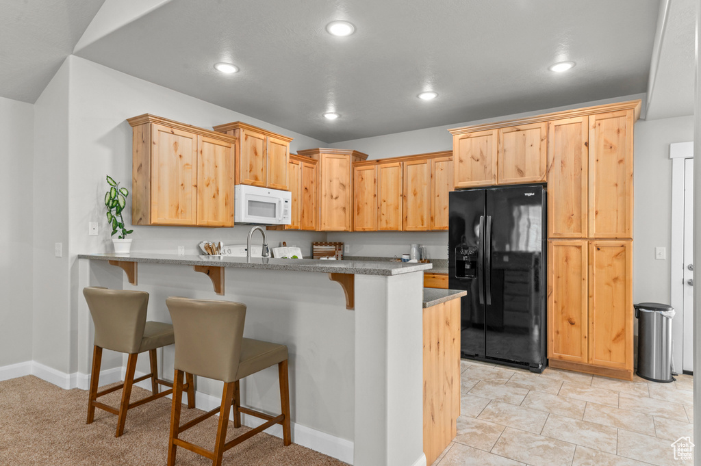 Kitchen with black fridge, white microwave, a kitchen breakfast bar, a peninsula, and recessed lighting