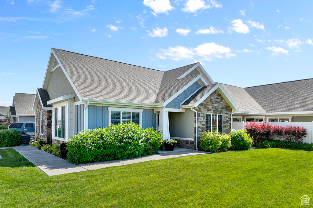 View of front of property with stone siding, a front lawn, board and batten siding, and a shingled roof