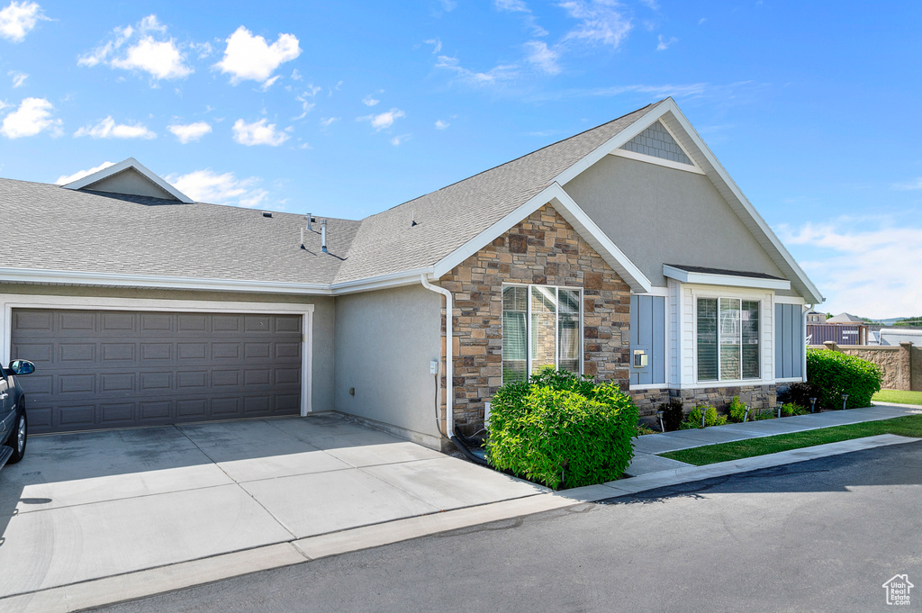 Craftsman-style home with stone siding, stucco siding, driveway, a garage, and roof with shingles