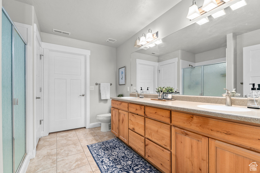 Full bathroom featuring double vanity, a shower stall, toilet, tile patterned flooring, and baseboards