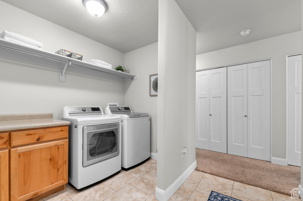Laundry area featuring washing machine and clothes dryer, baseboards, light tile patterned floors, and cabinet space