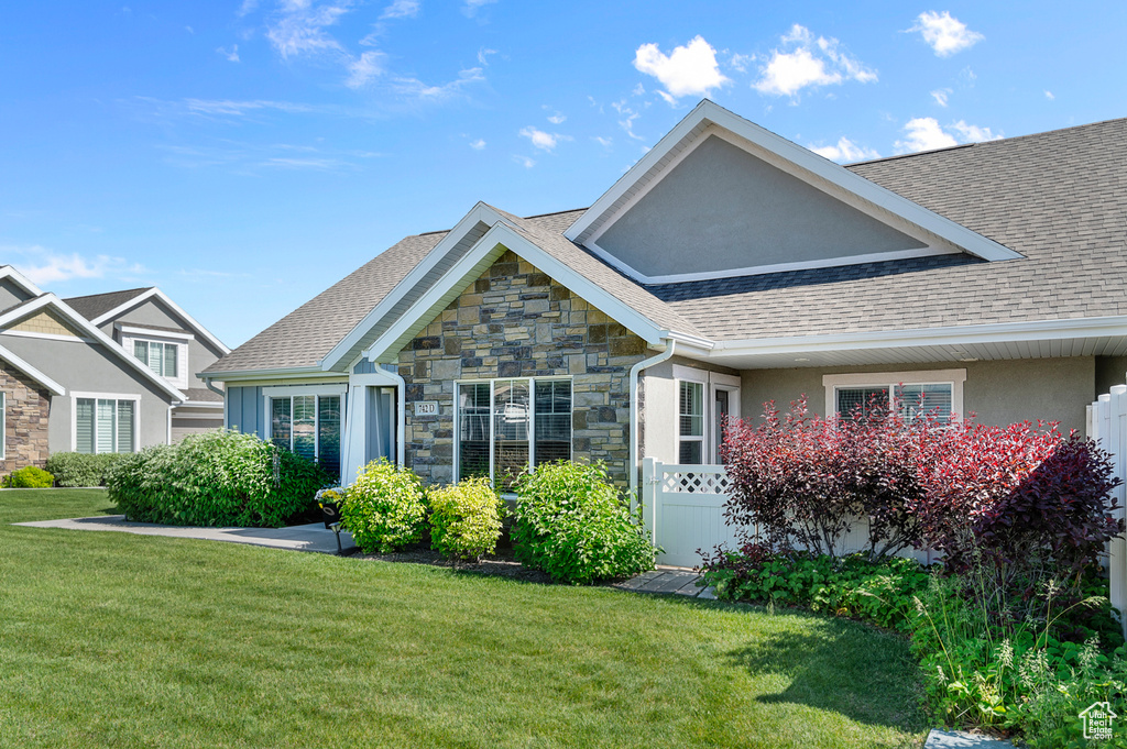 View of front facade featuring stone siding, a front yard, and roof with shingles