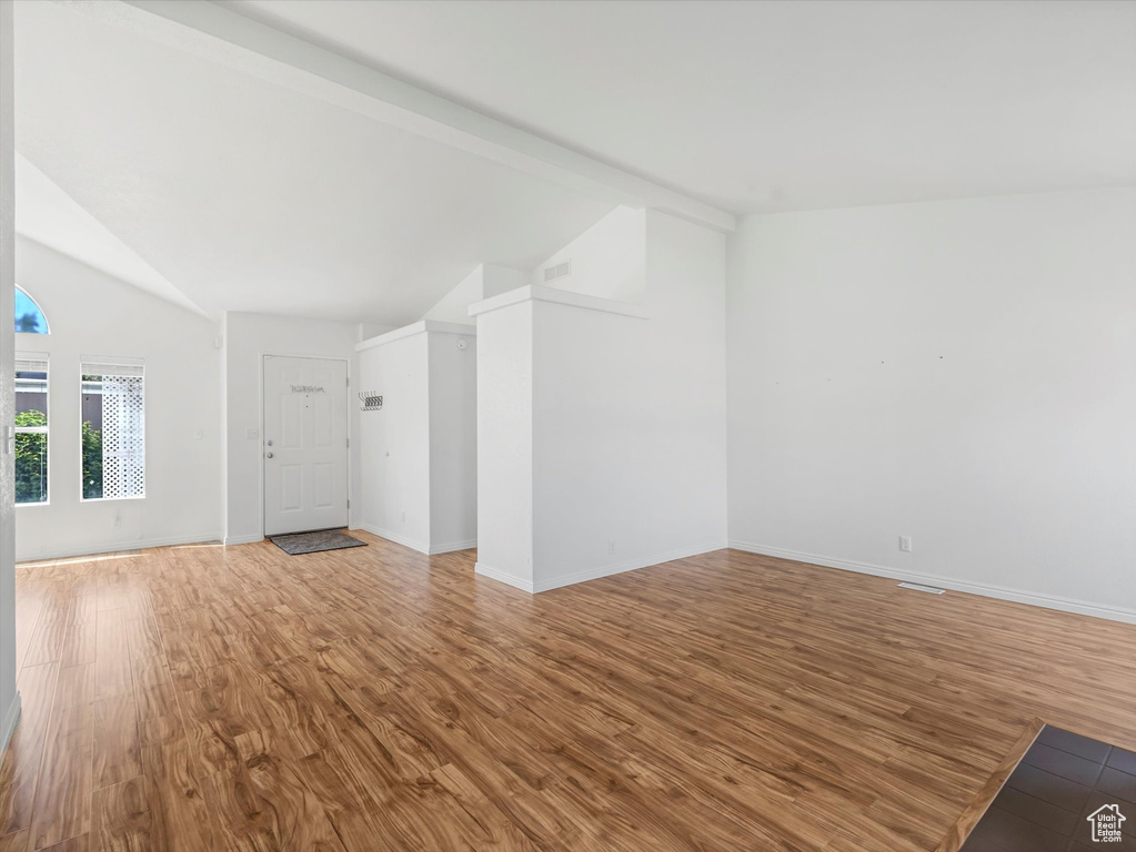 Unfurnished living room featuring lofted ceiling, wood finished floors, and baseboards