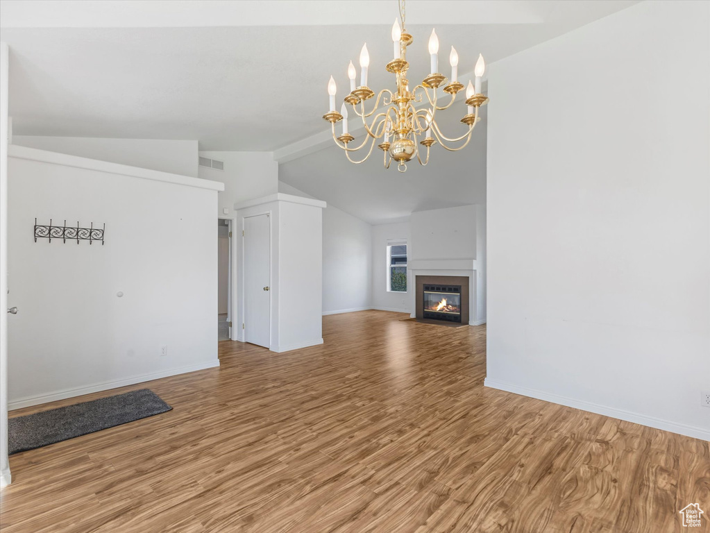 Unfurnished living room with lofted ceiling, wood finished floors, baseboards, a fireplace with flush hearth, and a chandelier