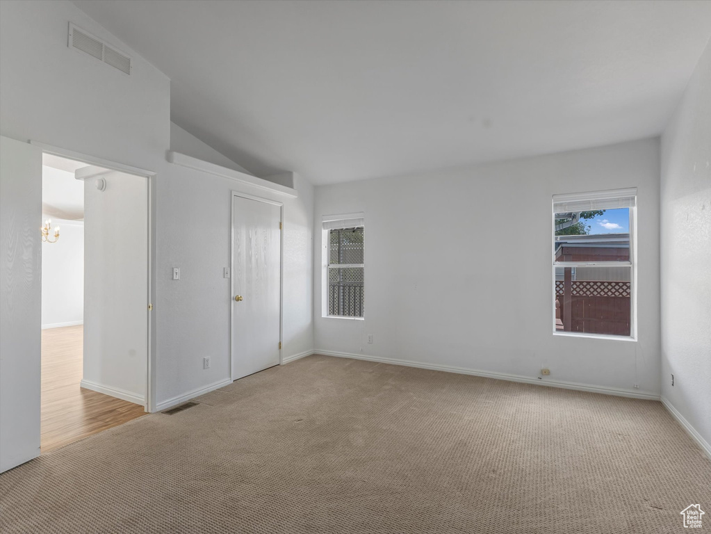 Unfurnished bedroom with light colored carpet, a chandelier, lofted ceiling, and baseboards